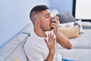 young-hispanic-man-using-inhaler-sitting-sofa-home